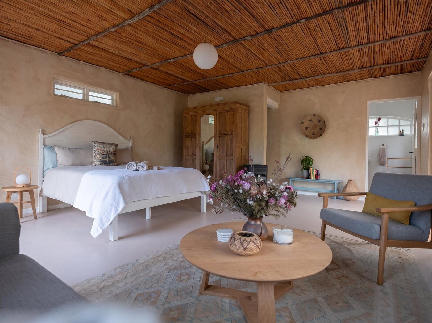 Inside the cottage: the bed, lounge chairs and flowers on the table under the bamboo ceiling